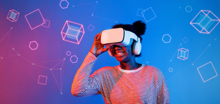 African girl with VR glasses standing at blue and pink background and looking at floating geometric...