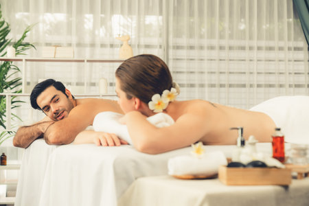 Blissful couple customer having exfoliation treatment in luxury spa salon with warmth candle light ambient. Salt scrub beauty treatment in health spa body scrub. Quiescentの写真素材