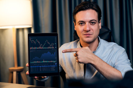 Smart business trader in casual looking at camera with pointing tablet in dynamic increased stock...