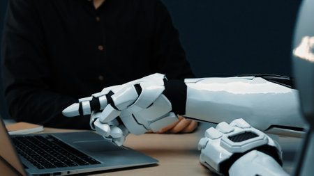 A close-up of a robot hand pointing at a laptop in a modern workspace, illustrating the collaboration between humans and advanced technology in todays digital world.の写真素材