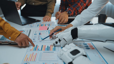 A modern office scene depicting collaboration between human hands and a robotic arm as they analyze business charts and graphs, showcasing the blend of technology and teamwork.の写真素材