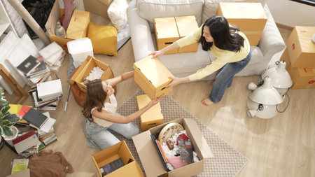 Top view of girl moving the box and sending to her roommate to place at living room surrounded with...