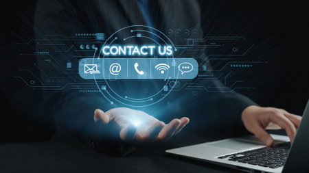 A businessman in a suit extends his hand towards digital contact icons floating above a laptop,...