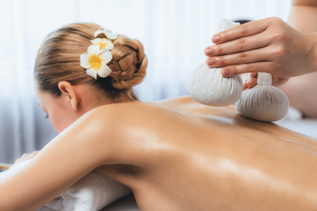 Hot herbal ball spa massage body treatment, masseur gently compresses herb bag on couple customer body. Tranquil and serenity of aromatherapy recreation in day lighting ambient at spa salon. Quiescentの写真素材