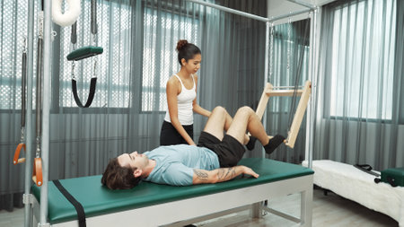 Skilled pilates instructor assisting a client in leg lift exercise on Cadillac equipment. Female trainer assist leg lift stretch on cadillac for improving core engagement, leg flexibility. Habituate.の写真素材