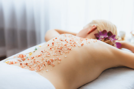 Woman customer having exfoliation treatment in luxury spa salon with warmth candle light ambient. Salt scrub beauty treatment in health spa body scrub. Quiescentの写真素材