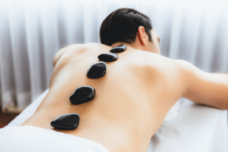 Hot stone massage at spa salon in luxury resort with day light serenity ambient, blissful man customer enjoying spa basalt stone massage glide over body with soothing warmth. Quiescentの写真素材