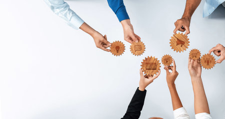 A diverse group of hands holds wooden gears symbolizing teamwork and collaboration. The scene...