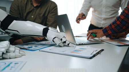 A human and a robotic hand work together in an office environment, interacting with technology and visual data, symbolizing collaboration and innovation in business.の写真素材