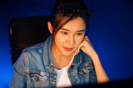 Stressful young beautiful asian creative looking on pc to search project creator social media online with planning channel strategy reach of more viewer home at neon modern office at night. Stratagem.の写真素材