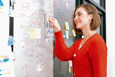 Professional attractive female leader sticks sticky note while presents creative marketing plan by...