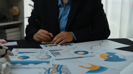 A focused businessperson reviews various data charts and graphs in a contemporary office setting,...