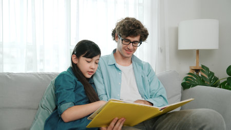 Happy daughter lean on father shoulder while listening story telling. Young asian schoolgirl looking...