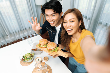 Top view of smiling host chef influencers taking photo with smartphone by selfie holding double hamburger on cooking show special easy with salad side dish homemade on social media channel.の写真素材