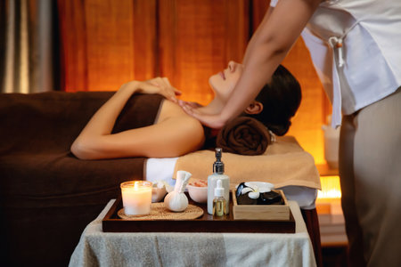 Aromatherapy massage ambiance or spa salon composition setup with focus decor candles and spa accessories on blurred woman enjoying blissful aroma spa massage in resort or hotel background. Quiescentの写真素材
