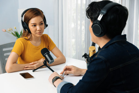 Smiling radio influencer host wearing headphone interviewing woman speaker sharing information to listeners on social media online website live streaming channel at morning at studio record. Infobahn.の写真素材