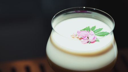 Closeup rotating in passion fruit smoothy cocktail glass serving special refreshing drink garnished with pink flower on smooth fizzy.の写真素材