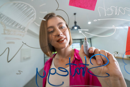Closeup of attractive smart caucasian businesswoman brainstorms and planing marketing idea by using mind map and colorful sticker on glass board. Creative start up business concept. Immaculate.の写真素材