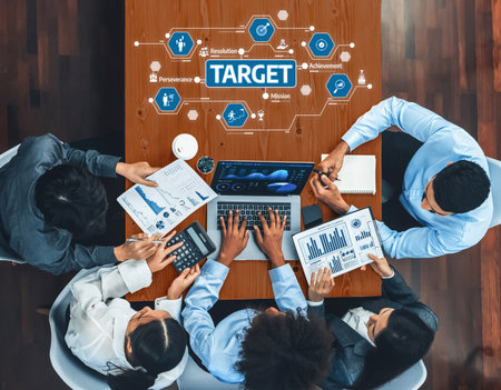 A diverse group of professionals engaged in a strategy session, analyzing data and discussing plans to achieve business targets, showcasing teamwork and collaboration.の写真素材