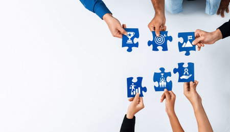 Hands holding colorful puzzle pieces with various business icons symbolize teamwork and...