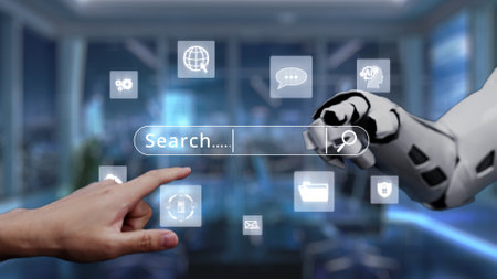 This image features a human hand touching a digital search bar alongside a robotic hand in a modern office, symbolizing the interaction between human and artificial intelligence. Auvanaの写真素材