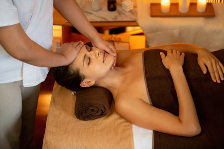 Caucasian woman enjoying relaxing anti-stress head massage and pampering facial beauty skin recreation leisure in warm candle lighting ambient salon spa in luxury resort or hotel. Quiescentの写真素材