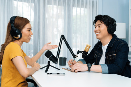 Smiling radio influencer host wearing headphone interviewing woman speaker sharing information to listeners on social media online website live streaming channel at morning at studio record. Infobahn.の写真素材
