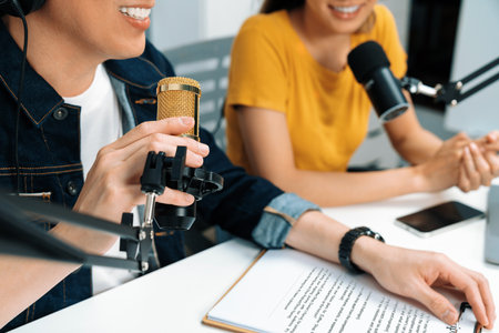 Cropped smiling radio influencer hosts wearing headphones with channel social media online live streaming talking topic on script note and laptop to listeners at morning at studio record. Infobahn.の写真素材