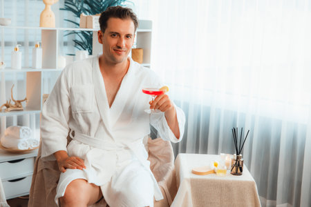 Beauty or body treatment spa salon vacation lifestyle concept with man wearing bathrobe relaxing with drinks in luxurious hotel spa or resort room. Vacation and leisure relaxation. Quiescentの写真素材