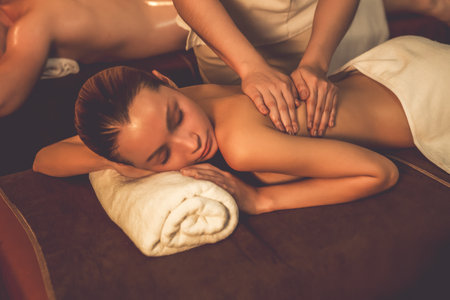 Caucasian couple customer enjoying relaxing anti-stress spa massage and pampering with beauty skin recreation leisure in warm candle lighting ambient salon spa at luxury resort or hotel. Quiescentの写真素材