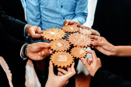 A diverse group of hands coming together to connect wooden gears, symbolizing collaboration and strategic planning in a modern business environment. Amityの写真素材