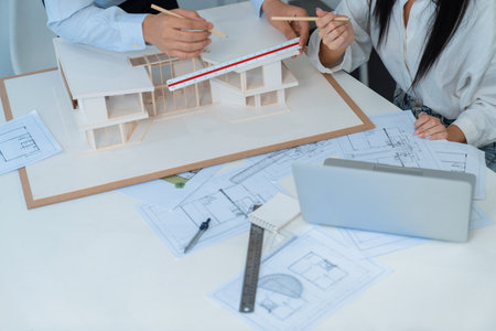 Professional engineer measures house model while skilled designer writes down in blueprint. Work...