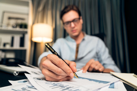 Thinking smart businessman surrounded paperwork report paragraph dynamic database analyzing to present customer target marketing analysis paper sheet for company meeting at home office. Pecuniary.の写真素材