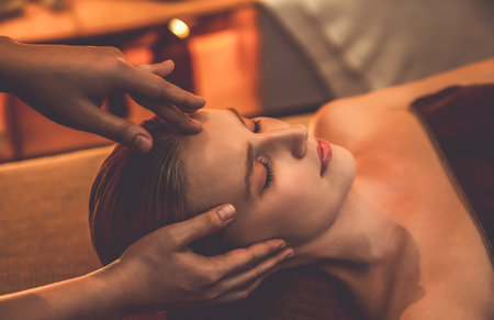 Caucasian woman enjoying relaxing anti-stress head massage and pampering facial beauty skin recreation leisure in warm candle lighting ambient salon spa in luxury resort or hotel. Quiescentの写真素材