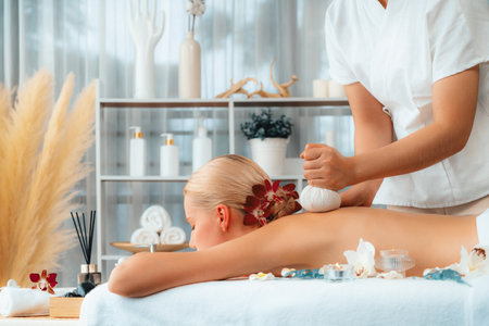 Hot herbal ball spa massage body treatment, masseur gently compresses herb bag on woman body. Tranquil and serenity of aromatherapy recreation in day lighting ambient at spa salon. Quiescentの写真素材