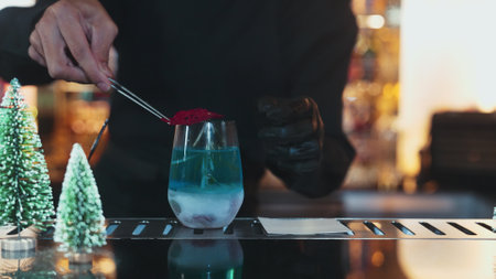 Bartender serving Christmas blue Lagoon cocktail with red dried fruit rosemary design on luxury bar counter with green neon snow Christmas tree festive.の写真素材
