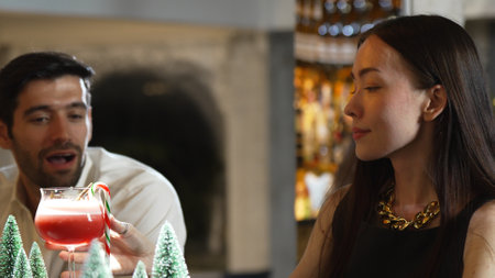 Smiling woman drinking punch cocktail garnished with candy cane cinnamon Christmas theme on luxurious counter bar talking with couple in lifestyle at decorated pine neon snow at nightclub. Vinosity.の写真素材