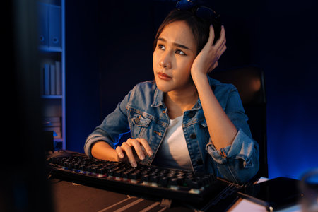 Stressful young beautiful asian creative looking on pc to search project creator social media online with planning channel strategy reach of more viewer home at neon modern office at night. Stratagem.の写真素材