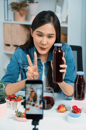 Smiling young beautiful Asian reviewing tasty mixed strawberry and cherry juice detox drinks, showing healthy product to promote for special promotion selling on social media online record. Stratagem.の写真素材