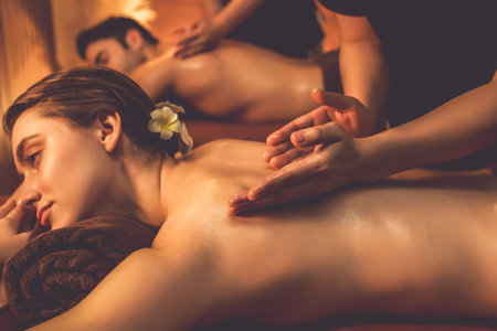 Caucasian couple customer enjoying relaxing anti-stress spa massage and pampering with beauty skin recreation leisure in warm candle lighting ambient salon spa at luxury resort or hotel. Quiescentの写真素材