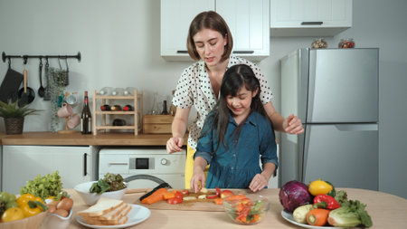 Smart caucasian mother and asian girl cooking together and chopping vegetable or preparing salad for dinner. Happy mom and daughter making healthy food with fresh food. Healthy food concept. Pedagogy.の写真素材