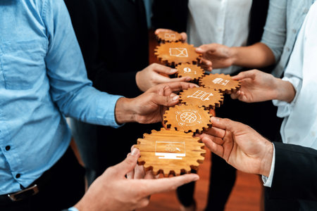 A group of professionals collaborates with wooden gears, illustrating business strategies and innovation in a modern corporate setting. Hands exchange ideas while fostering unity. Amityの写真素材