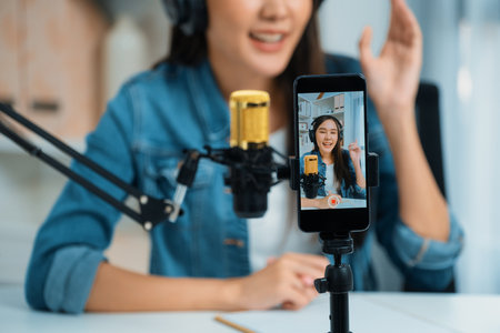 Host channel Asian influencer talking in broadcast wearing headsets on social media live on smartphone recording online, greeting listeners with coaching life or business at modern studio. Stratagem.の写真素材