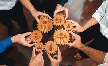 This image showcases a diverse group of hands positioning wooden gears, each with unique symbols, representing teamwork and collaboration within a professional environment. Amityの写真素材