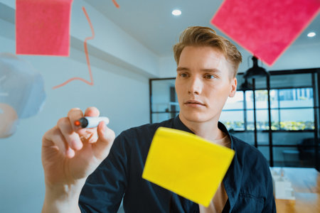 Professional caucasian businessman writing marketing idea by using mind map and sticky notes on glass board at modern meeting room. Creative business and planing concept. Closeup. Immaculate.の写真素材