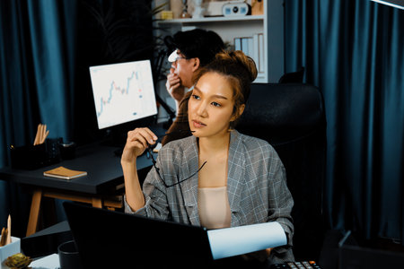 Businesswoman looking outside with thinking report data analysis overworked project job while holding glasses with coworker working at back side at over late night time at modern office. Infobahn.の写真素材