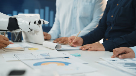 A diverse business team engaged in collaborative work with the assistance of a robotic arm, analyzing data and strategizing in a modern office setup.の写真素材