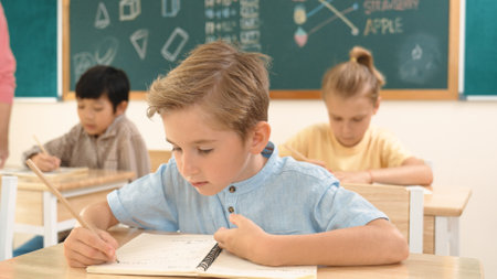 Attractive caucasian boy looking at camera while studying math at school. Diverse cute student doing test while teacher asking asian child question and point at paper in front of blackboard. Pedagogy.の写真素材