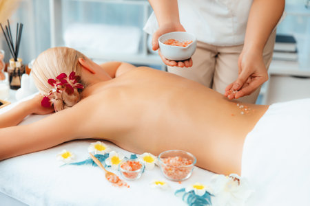 Woman customer having exfoliation treatment in luxury spa salon with warmth candle light ambient. Salt scrub beauty treatment in health spa body scrub. Quiescentの写真素材