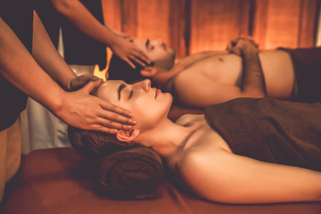 Couple customer enjoying relaxing anti-stress head massage and pampering facial beauty skin recreation leisure in warm candle lighting ambient salon spa in luxury resort or hotel. Quiescentの写真素材